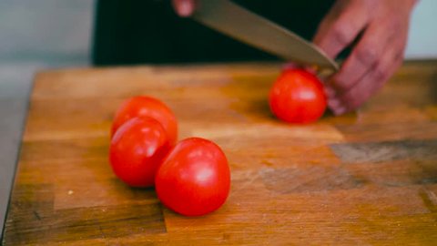 Close up of Italian male dicing tomatoes and placing them on a white plate