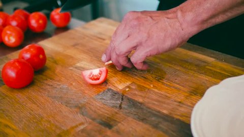 Close up of a Caucasian man cutting tomatoes with a knife and placing them on a white plate