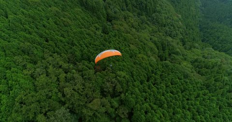 Aerial close follow shot of paraglider flying over the lush Japanese mountain ridges
