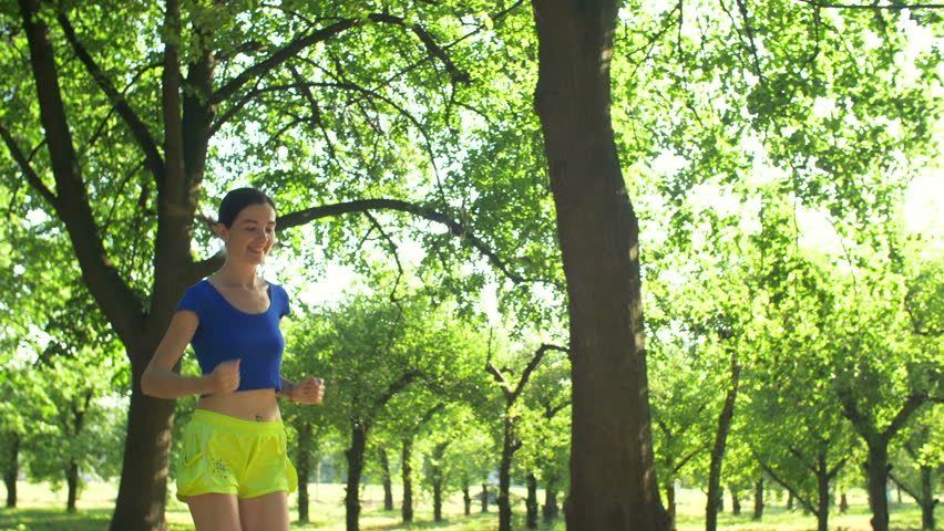 Positive healthy active brunette woman with ponytail jogging in summer park. Sport fitness woman running on summer day during training and exercising outdoors over natural landscape background.