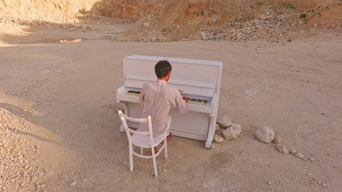 young man plays the piano on a background of yellow mountains and stones