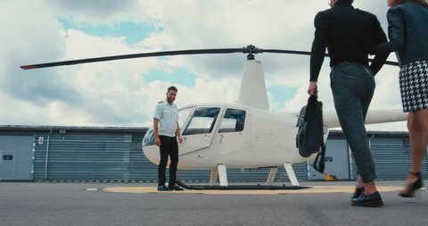 Commercial pilot in uniform greeting clients near small private helicopter on a landing point. 4K UHD