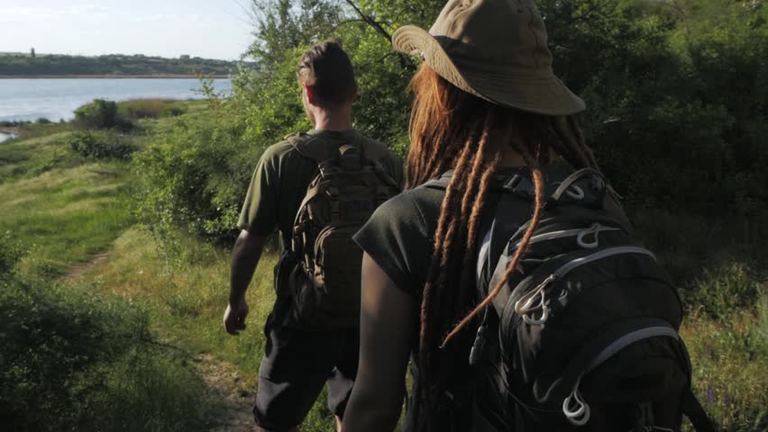 Couple of backpackers travel near river in summer sunny day 