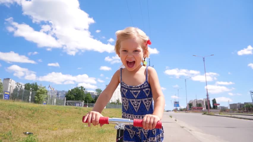 Little girl quickly rides Kick scooter along path in summer country side park. Slow Motion