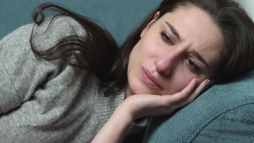 Lonely depressed youn woman crying lying on the couch