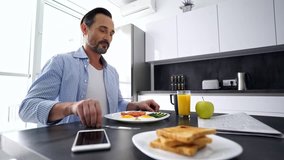 Smiling mature man having tasty healthy breakfast at the kitchen table