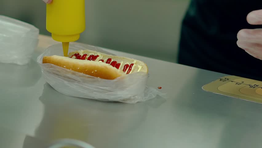 CU, Slow motion: Cook is preparing a hot dog, watering it with mustard. 