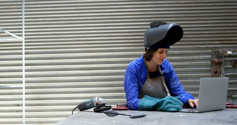 Young female welder using laptop in workshop 4k