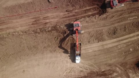 Aerial drone footage (top view) of a construction site.  Heavy equipment is grading the land, moving and flattening out red clay soil.
