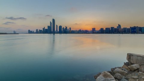 Abu Dhabi city skyline on sunrise time with water reflection timelapse from the Breakwater near cultural village. Few clouds on morning sky