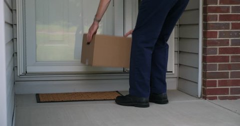 A delivery man places a cardboard box on a home's front porch then rings the doorbell before leaving.  	