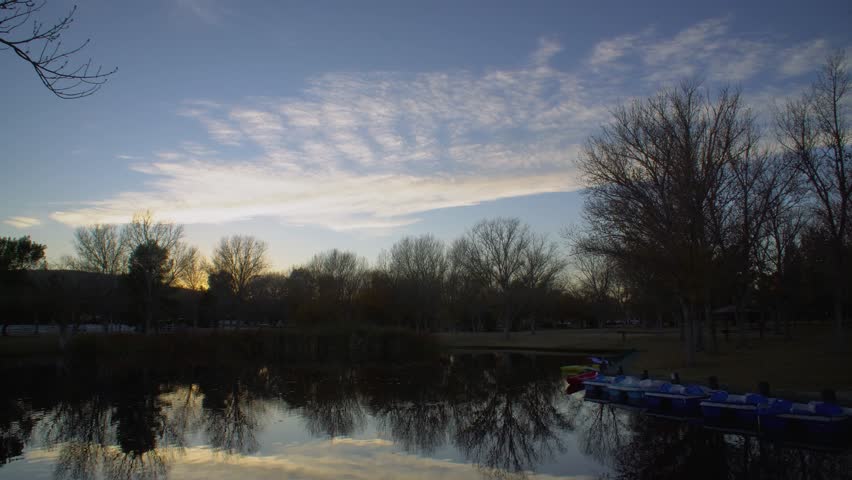 Time lapse of clouds over a lake with paddle boats in it at sunset