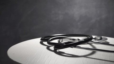 Stethoscope on a white table, dark wooden background, rotation 360 degrees.