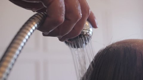 Women's hair being washed by a hairdresser with a shower head and water. The shower head and water are the main focus with the woman in the background. 4K UHD 16:9