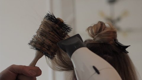 Hairdresser blowdrying and styling a blonde woman's long hair with a brush and hair dryer. Medium shot. 4K UHD 16:9
