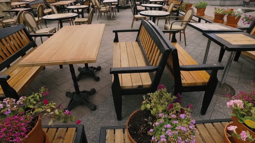 Summer outdoor cafe outdoor in the city in a summer sunny day. Tables and chairs made of wood in a cafe without people. The camera moves along the tables