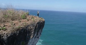 Aerial drone shot of pretty girl standing on the cliff with amazing ocean and cloudy sky view - video in slow motion