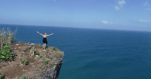 Aerial drone shot of pretty girl standing on the cliff with amazing ocean and cloudy sky view - video in slow motion