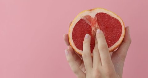 Female hand stroking fruit imprinting a petting close-up on a pink background. 