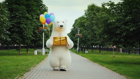 A large polar bear walks down the street, carries balloons and a box with a gift. Birthday gifts and a cool party concept
