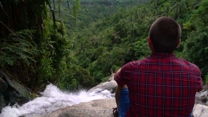 A man is sitting on the top of a waterfall