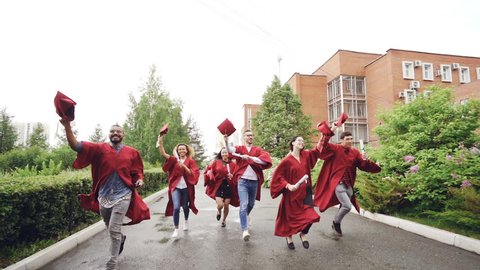 Slow motion of merry graduates running, holding diplomas and waving mortarboards enjoying freedom. Higher education, youth and happiness concept.