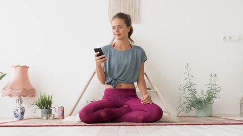 fitness, technology and healthy lifestyle concept - woman with smartphone meditating at yoga studio