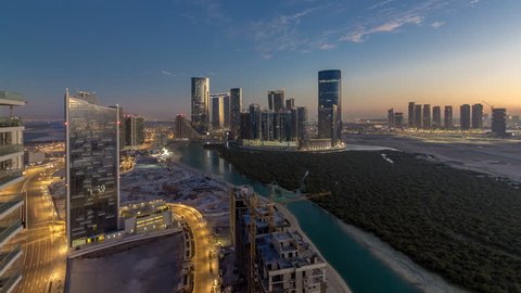 Skyscrapers on Al Reem and Al Maryah Island in Abu Dhabi day to night transition timelapse after sunset from above. Aerial citiscape from Al Reem Island with illuminated buildings