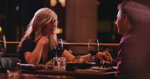Mature couple holding hands, flirting and having fun on dinner date night at gourmet restaurant