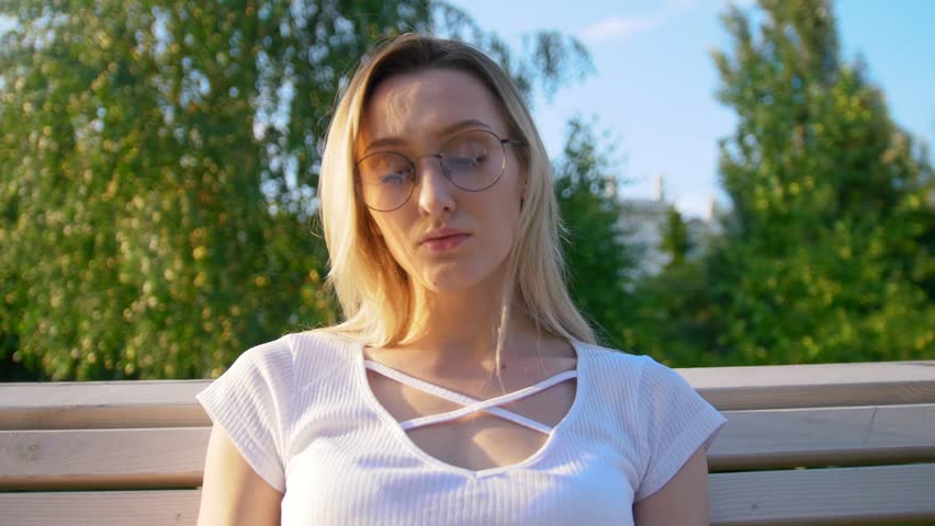 Pretty young woman reading a book on the bench outdoors at sunset