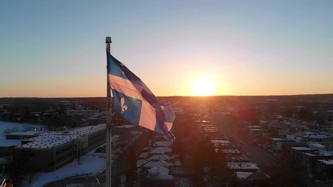 Slow motion drone view of the Quebec flag, with the sunset in the background