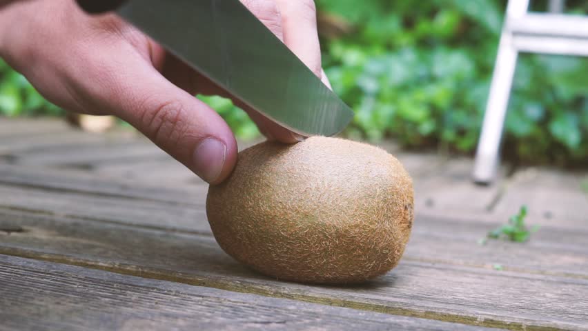 Raw cut of a fresh kiwi with a razor sharp knife, revealing the green interior.