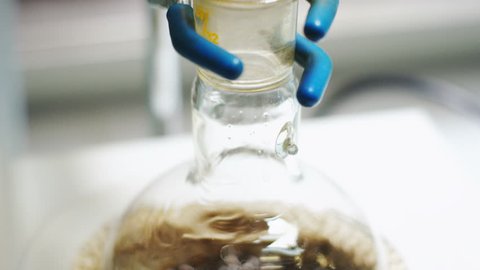 Closeup clear liquid flows down along lab glass bulb wall into oil boiled in hot modern oil distiller at plant