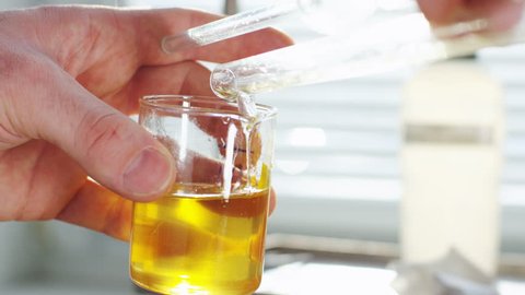 Closeup professional scientist pours clear yellow liquid extracted from oil into lab glass in refinery factory laboratory