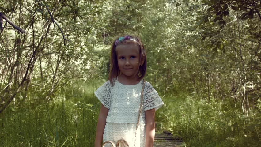 Little girl walks in the park. Young girl with white dress walking onto a mysterious path in the forest. Girl on old wooden brdge in forest. 