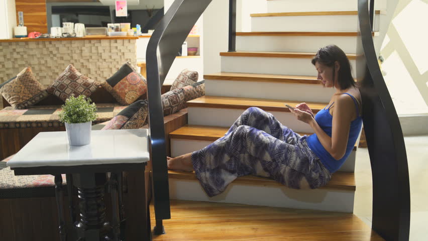 A girl with a smartphone sits on the stairs in the house. The man goes down the stairs Royalty-Free Stock Footage #1013232902