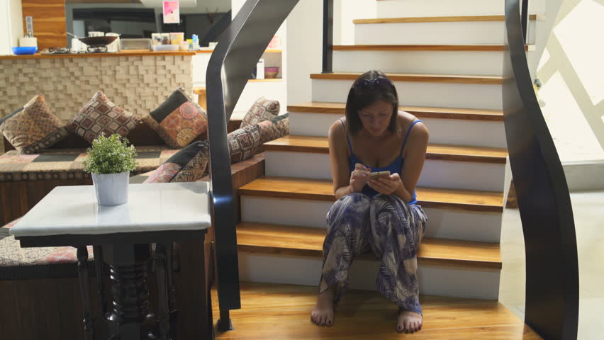 Woman sits on a stairs in the house and uses a smartphone. Man comes down the stairs and hugs a girl Royalty-Free Stock Footage #1013232914
