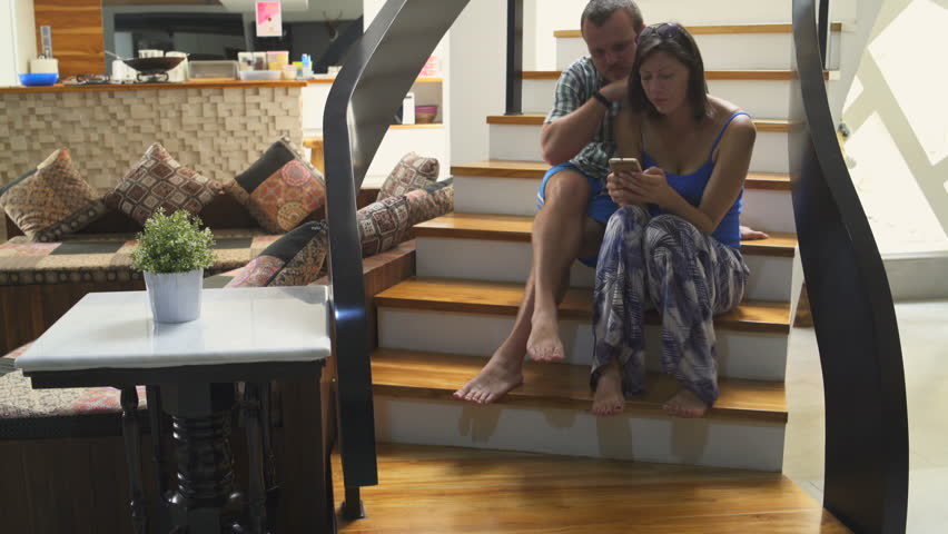 A man and a woman are sitting on the stairs in the house and using a smartphone Royalty-Free Stock Footage #1013232917