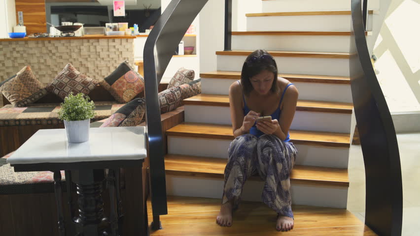 A woman sits on the stairs in the house and uses a smartphone. A man climbs the stairs Royalty-Free Stock Footage #1013232920