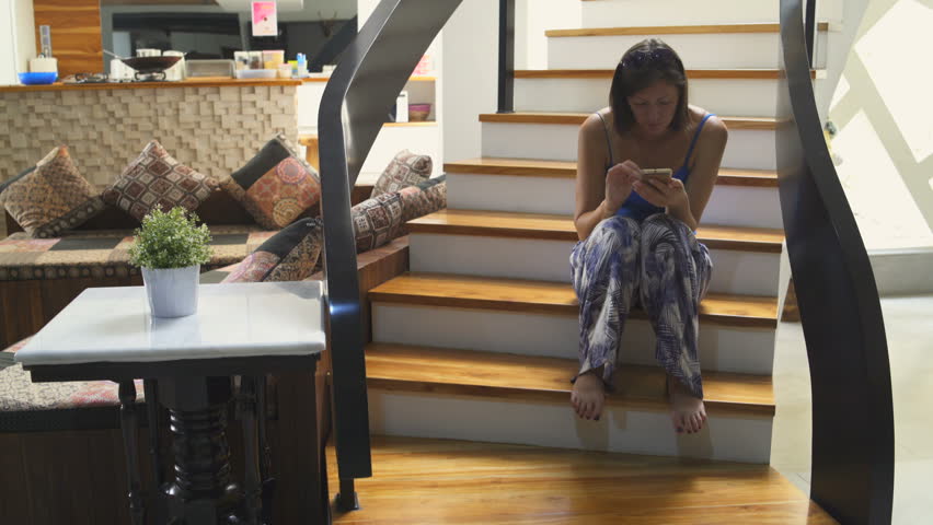 A woman is sitting on the stairs in the house with a smartphone Royalty-Free Stock Footage #1013232923
