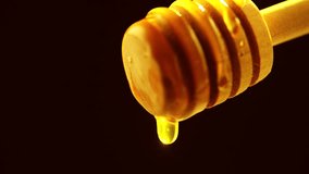 Honey dripping from honey dipper on black background. Healthy organic Thick honey dipping from the wooden honey spoon. 4K UHD video footage 3840X2160. On black background