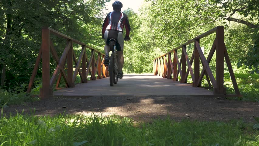 A man is riding a bicycle across the bridge in the park. slow motion
