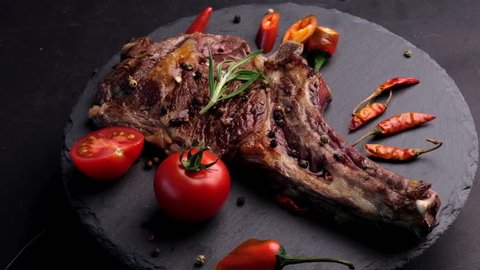 Grilled beef steak on bone with tomatoes rotating on the stone cutting board