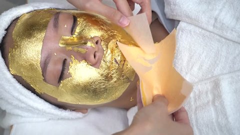 Young woman getting 24 karat gold facial treatment at the beaty clinic. The treatment of using real gold for youthful skin