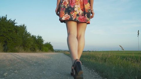 beautiful, attractive European girl with long leggs in short skirt with flowers walks in black heels along the road with gravel,the bottom view, slow motion
