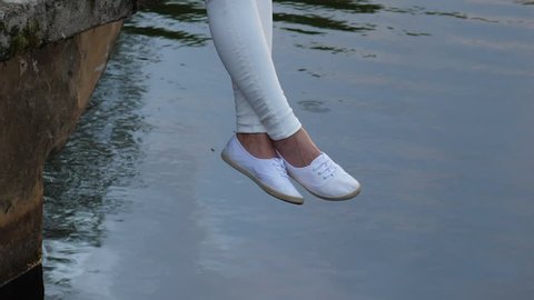 Female legs in white shoes swing over still water