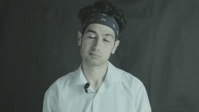 guy in a white shirt and bandana speaks and actively gestures on a black background