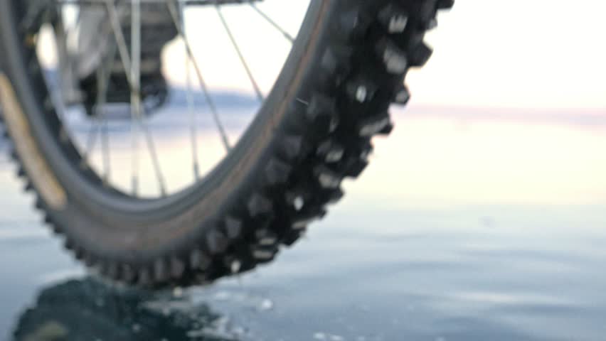 View of the tire. Shooting 180fps. Woman is riding bicycle on the ice. Ice of the frozen Lake Baikal. The tires on the bicycle are covered with special spikes. The traveler is ride a cycle. | Shutterstock HD Video #1013258786