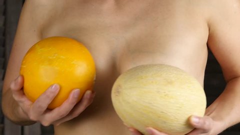 Young happy woman holds two melons above her breast. Plastic surgery and silicone implants concept. 4K
