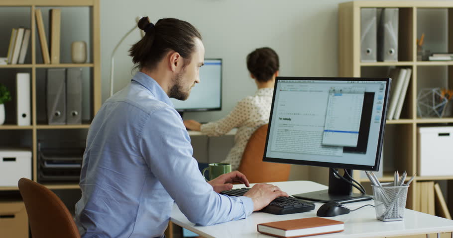 Rear of the male nervous Caucasian office worker typing and texting on the laptop computer while it being broken and has error writing on the screen. Indoors.